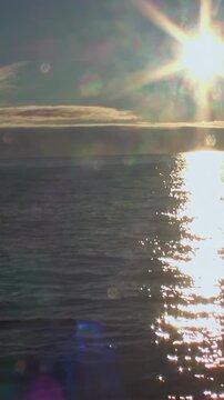 Witness the serene beauty of the Arctic. The sun descends, casting a brilliant, dancing light across the vast, tranquil ocean surface. Wispy clouds line the horizon in this peaceful, golden moment.