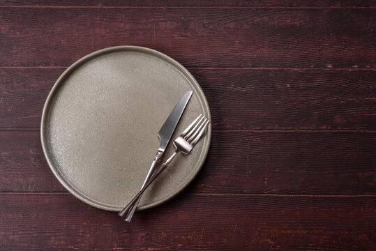 An empty round ceramic plate on a dark, textured brown background. An empty round plate