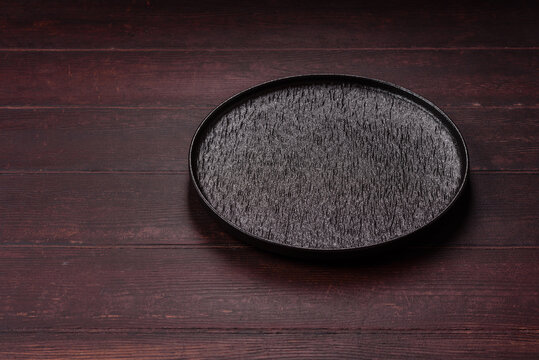 An empty round ceramic plate on a dark, textured brown background. An empty round plate