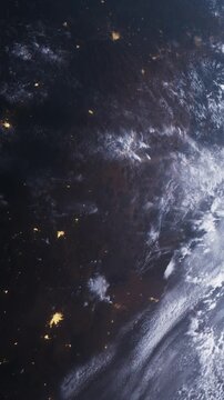 Earth at night with lights from cities shining brightly. Clouds move across the surface. The view captures the planet from high above in space.