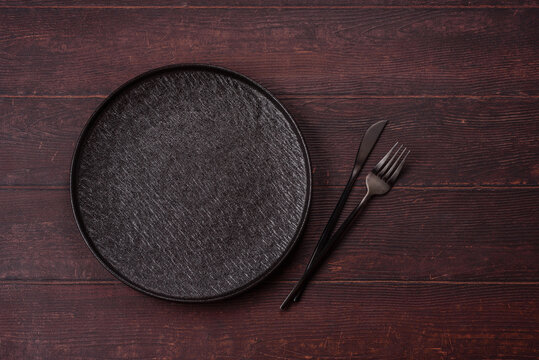 An empty round ceramic plate on a dark, textured brown background. An empty round plate