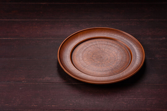An empty round ceramic plate on a dark, textured brown background. An empty round plate