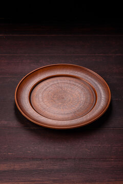 An empty round ceramic plate on a dark, textured brown background. An empty round plate