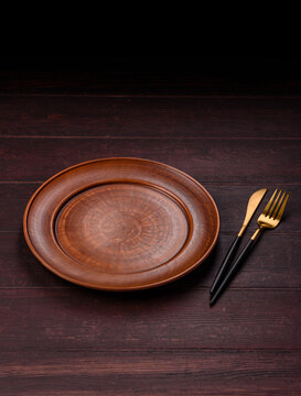 An empty round ceramic plate on a dark, textured brown background. An empty round plate
