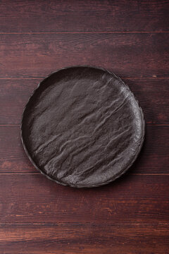 An empty round ceramic plate on a dark, textured brown background. An empty round plate
