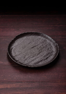 An empty round ceramic plate on a dark, textured brown background. An empty round plate