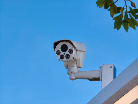 White security camera mounted on building exterior wall. Outdoor surveillance system for monitoring safety and crime prevention.