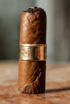 Handcrafted premium cigar with a golden band standing upright on a textured surface, luxury tobacco product, the cigar features a detailed brown wrapper leaf