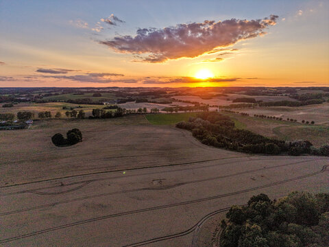 aerial sunset over rolling agricultural countryside with golden fields and dramatic evening sky