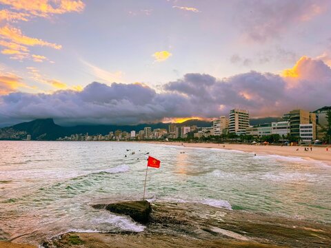 Dusk on Ipanema beach in Rio de Janeiro with the city lights on and the sky colored by the sunset reflecting in the sea water