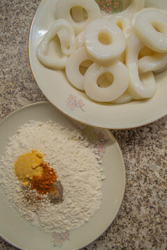 High angle view of hand coating fresh raw squid rings in seasoned flour next to breadcrumbs. Step-by-step preparation for making crispy fried calamari rings at home. Ideal for seafood recipes, culinar