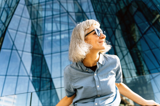 Smiling woman in sunglasses by modern glass office building