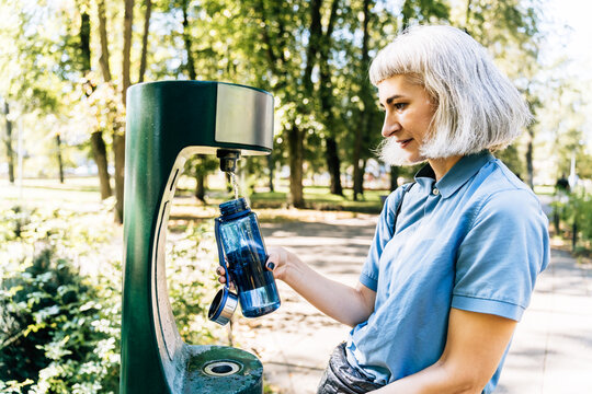 Woman refilling reusable bottle at park water fountain