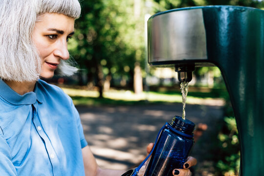Woman filling reusable bottle at public water fountain