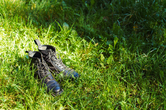 Pair of black leather boots on green grass in sunlight