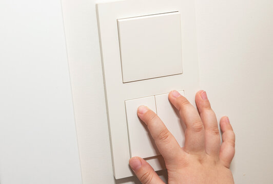 Hand pressing modern light switch on white wall. Home electricity control
