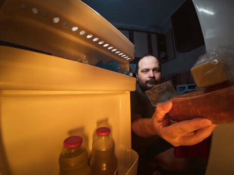 Man takes groceries from refrigerator in home kitchen