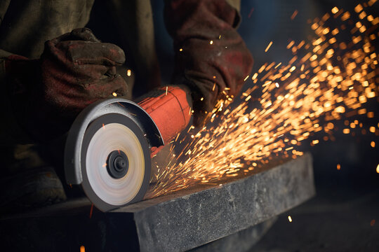 Worker cuts stone with angle grinder and flying sparks