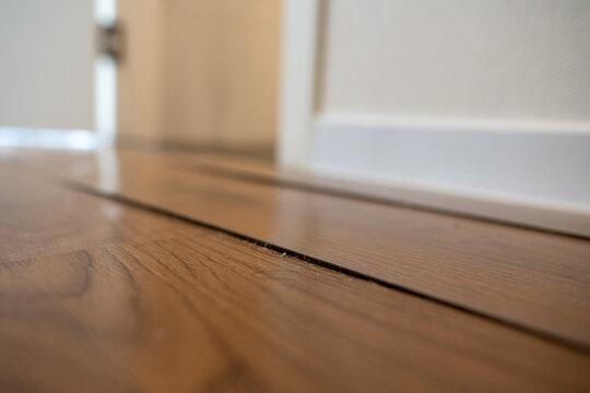 Water-damaged laminate flooring with a swollen, uneven seam between two wood-grain planks