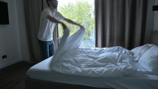 Man making his bed, tidying up the bedroom during a morning household routine