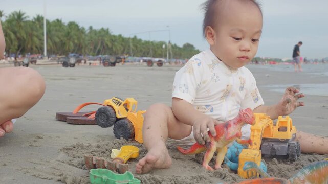 A young child enjoys playing with colorful toy vehicles on the sandy beach, surrounded by a serene coastal atmosphere.