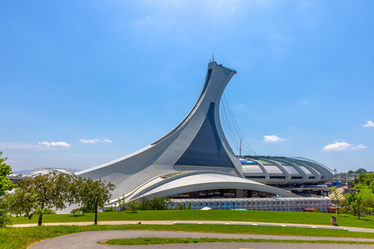 Montreal, QC, Canada. Aug 1, 2026. Wide angle view of Olympic Stadium and Montreal Tower rising above green park against clear blue sky.
