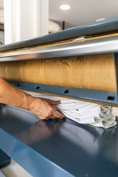 Worker loading folded linen into industrial ironing press