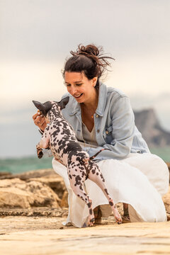 Woman playing with spotted dog on rocky shore at sunset