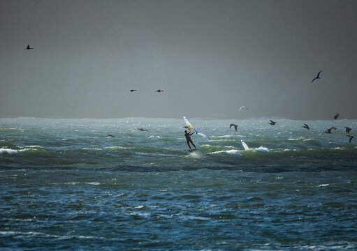 Windsurfer riding rough West Coast waves under gray sky