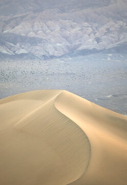 Wind-sculpted sand dune with desert mountains, West Coast