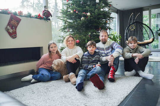 Family relaxing by decorated Christmas tree at home