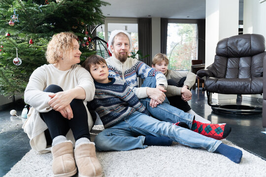 Family relaxing by Christmas tree in cozy living room