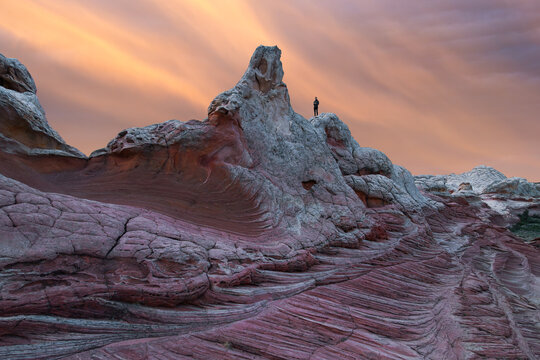 Lone hiker on White Pocket sandstone at sunset sky