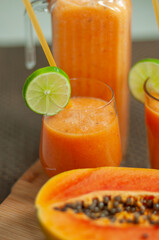 Homemade papaya smoothie with fresh lime garnish in serving glasses beside a ripe papaya. Refreshing tropical drink prepared from fresh fruit for healthy lifestyle and wellness concepts. © Anna Zaro