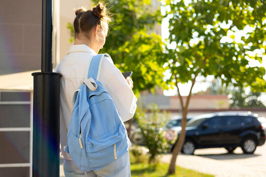Teenage student with school backpack using smartphone outdoors, back to school lifestyle 