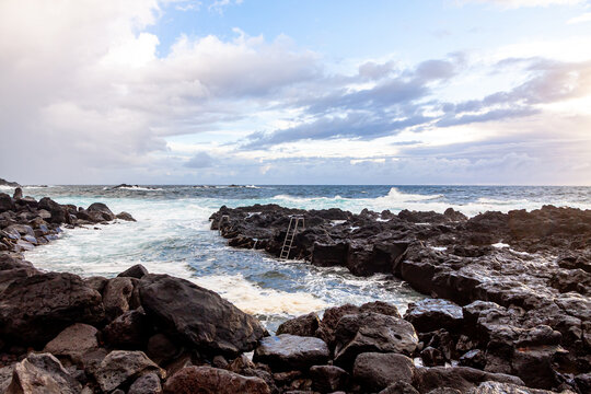 Scenic view of Ponta da Ferraria natural swimming area on Sao Miguel Island, Azores, Portugal, with rugged lava rocks, Atlantic waves and cloudy sky