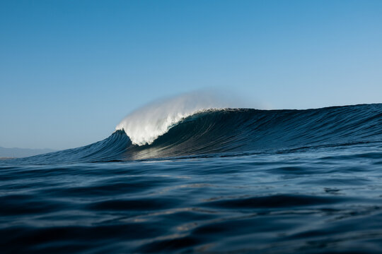 Powerful ocean wave cresting under clear blue sky