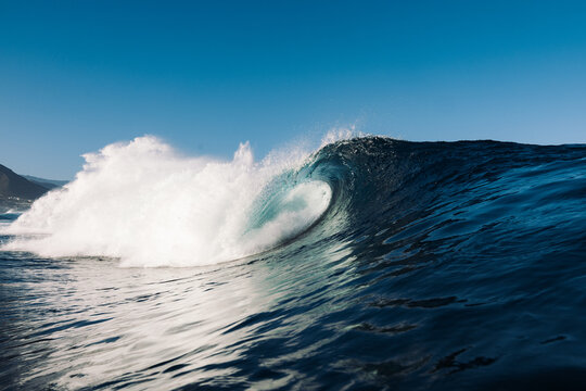 Powerful ocean wave curling and crashing under blue sky