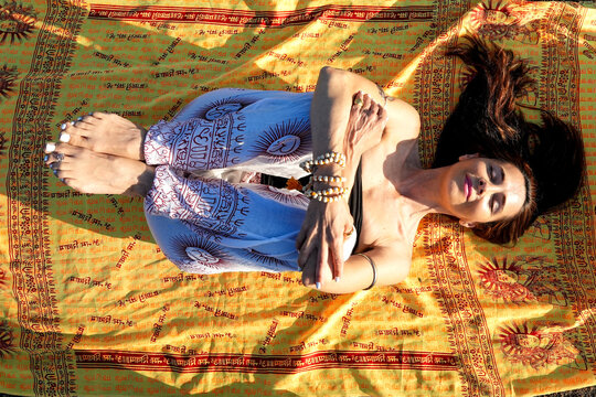 Woman meditating in yoga pose on patterned mat outdoors