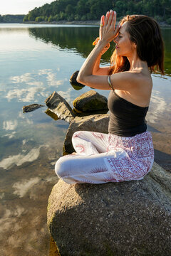 Woman practicing yoga by a calm lake at sunrise