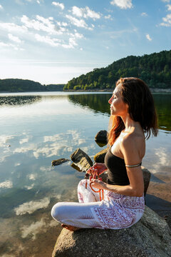 Woman meditating by a calm lake for yoga wellness balance