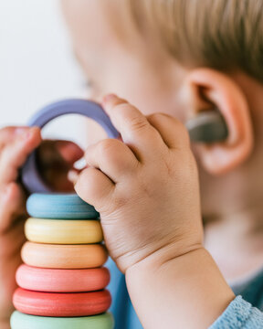 Cochlear implant child playing with wooden ring toy, soft daylight, warm skin tones, copy space