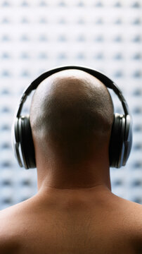 Soundproof booth back view headphone acoustic panel head neck skin person studio test soundproof booth vertical close up rear shoulder bald listening audio sound equipment headset earcup black