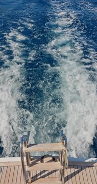 seething water from under a moving catamaran, crystal clear azure water, sea foam, ladder with ladder for descent into the water, wooden deck