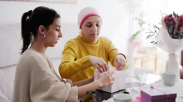 Daughter supporting mother with cancer wrapping gift together