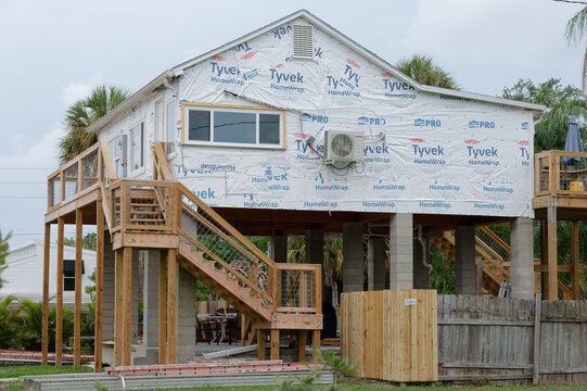 An elevated coastal house under construction wrapped in Tyvek weather barrier on concrete pilings. Editorial Use Only August 1, 2026 Gulfport ,FL USA. Featuring wooden staircases, an outdoor deck and 