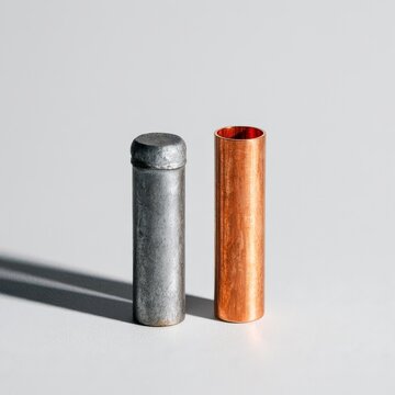 Two pipe sections stand on a pale grey surface with long shadows and bright light from the left side