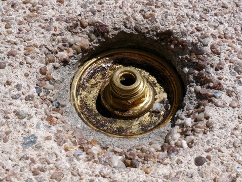 Brass curb stop installed in concrete sidewalk with cover open under bright sunlight