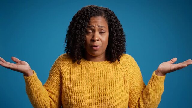 Confused woman shrugging with open hands against a blue background