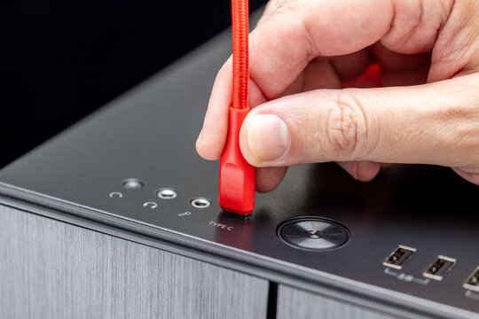 A hand holds a red braided cable inserted into a Type-C port marked TYPE C on the top panel of a PC case. The black panel shows a round power button, USB ports, and audio jacks.